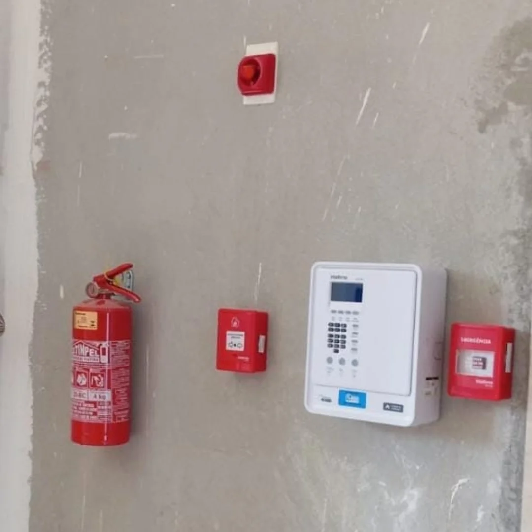 Conjunto de extintor, acionador, central de alarme e sirene instalados em parede