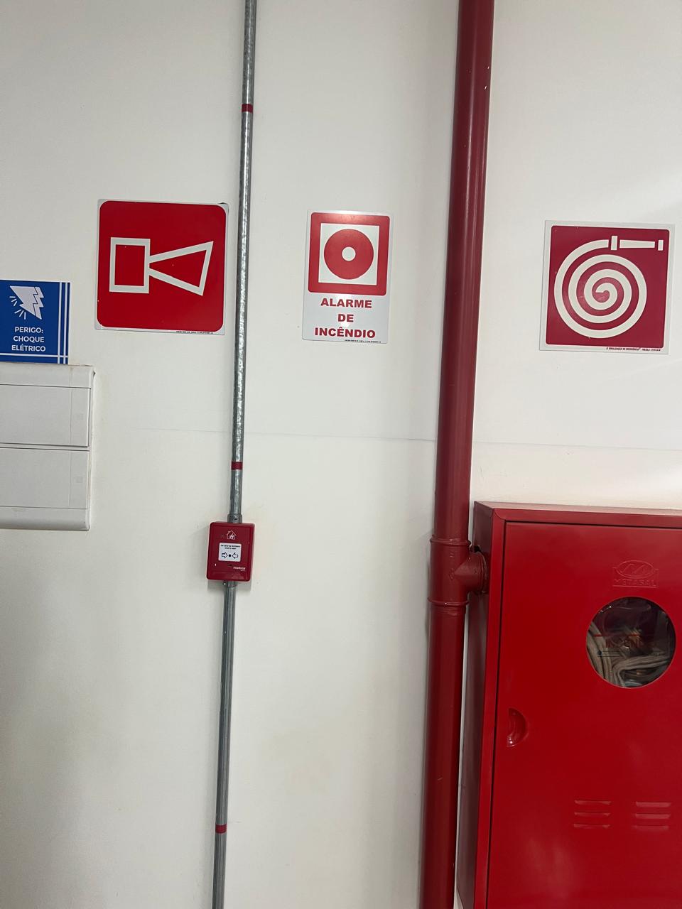 Conjunto de placas fotoluminescentes de alarme, hidrante e mangueira ao lado de abrigo